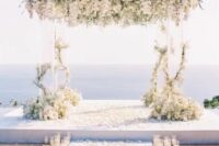 44 a breathtaking wedding ceremony space with a sea view, an acrylic arch with lush white florals, pillar candles lining up the aisle