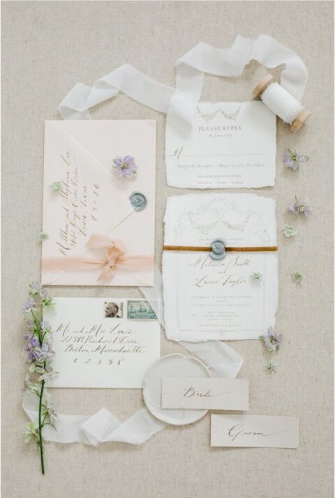 a neutral wedding invitation suite with a blush envelope, gold calligraphy and irregular-shaped pieces, white fabric ribbon