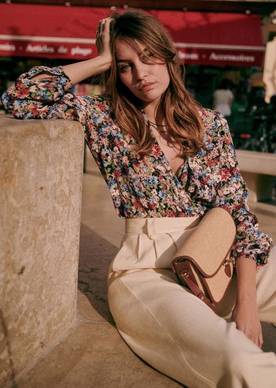a bold floral wrap blouse with short sleeves, creamy high waisted pants and a small bag are a cool combo for a casual summer wedding