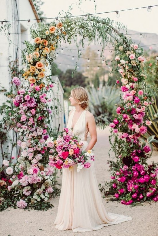 a bright ombre floral wedding arch with light and pale pink, orange and peachy, blush and hot pink blooms and greenery is wow