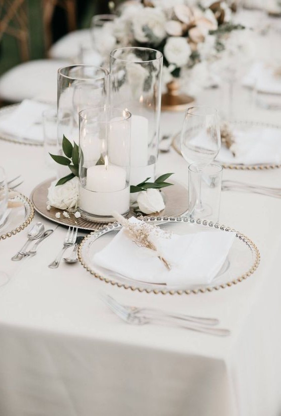a refined wedding tablescape with metallic trays with candles and blooms, sheer chargers and neutral linens with dried blooms