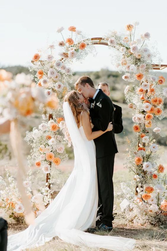 a chic and catchy wedding arch with white, blush ad orange blooms delicately covering the arch is a lovely and effortlessly chic idea