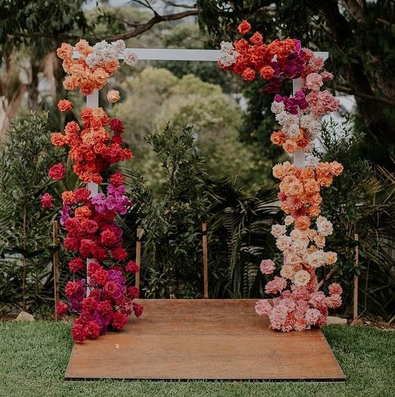 a colorful floral wedding arch with blooms of hot pink and light pink, red, orange, white, peachy pink colors looks spectacular
