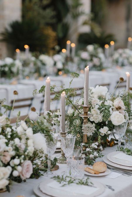 a romantic wedding table setting done with lush white and blush blooms and greenery, grey tall and thin candles, white porcelain and elegant glasses