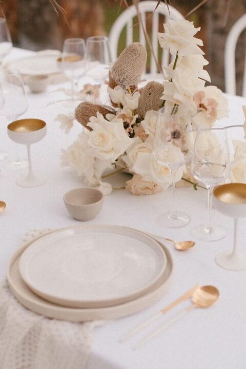 a warm neutral wedding tablescape with neutral linens, neutral florals, gold and creamy glasses, neutral plates and gold cutlery