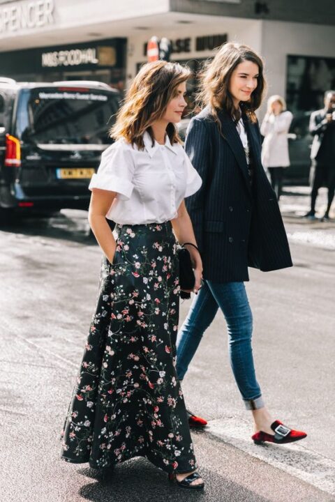 a pretty wedding guest look with a white shirt with short sleeves, a refined black maxi skirt with pink floral prints, black shoes and a black bag