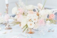 52 an airy summer wedding table setting with white linens and porcelain, gold and white cutlery, a lush neutral floral centerpiece and tall and thin candles