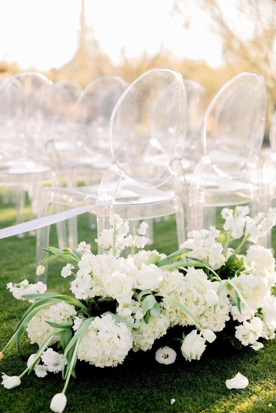 modern lux wedding ceremony space decor done with white blooms and ghost chairs is simple and very chic