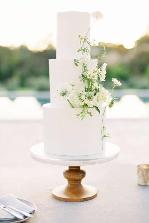 a beautiful white wedding cake decorated with some white wildflowers is a messy and lovely idea for a summer wedding