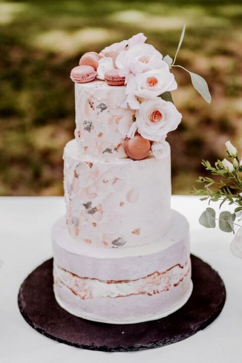 a blush fault line wedding cake with painted pink blooms, coral macarons, white blooms and greenery for a summer wedding