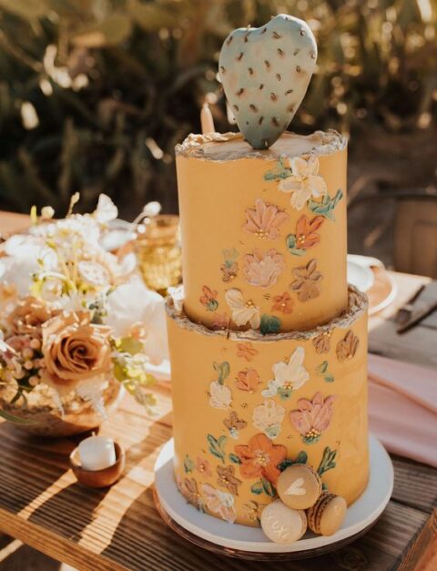 a cool marigold floral painted wedding cake with macarons and a sugar cactus for a boho desert wedding