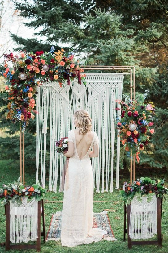 a macrame wedding backdrop with bright orange, burgundy, peachy pink and blue flowers plus greenery