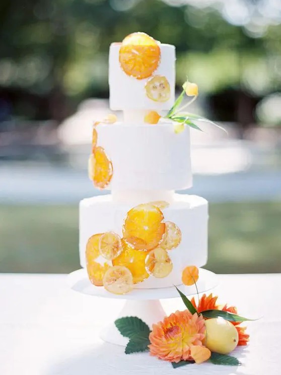 a creative white wedding cake with dried citrus slices and some blooms is a cool and bold wedding dessert