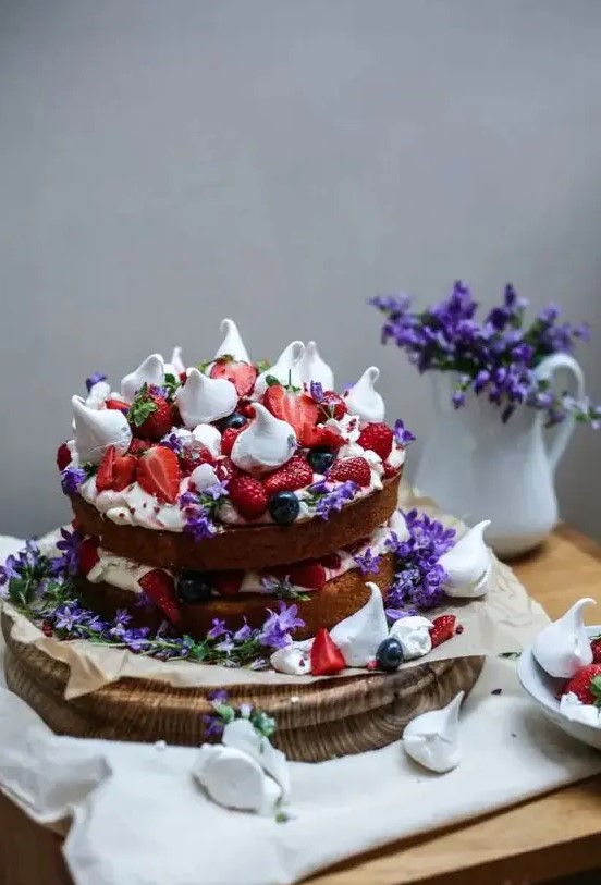 a bold naked sponge cake with strawberries, raspberries, meringues and purple flowers for a mid summer wedding