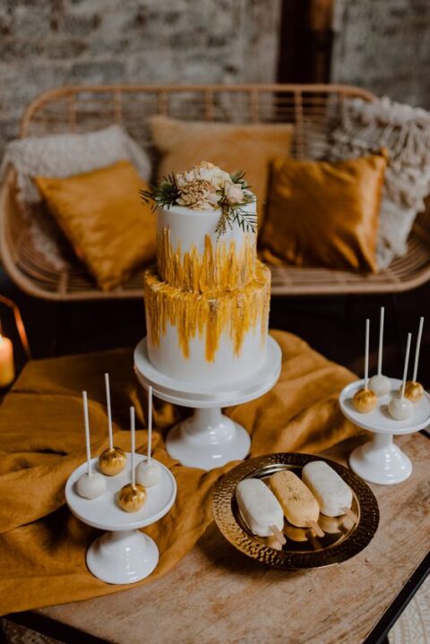 a delicious boho wedding desserts bar with a wedding cake with marigold textural patterns and gold and white sweets