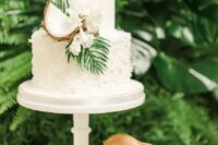57 a white plain and textural wedding cake decorated with white blooms, greenery and coconuts for a tropical wedding