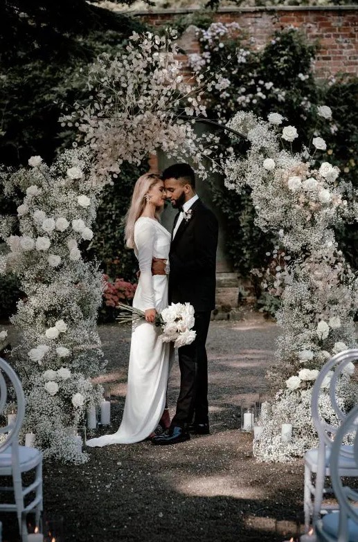 a sophisticated and airy wedding arch covered with white roses and baby's breath plus some bloomign branches on top is amazing