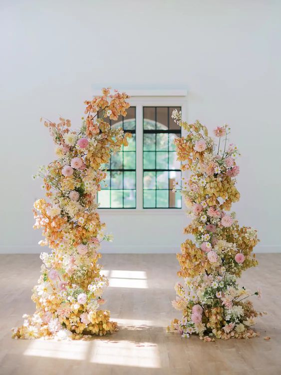 a vivacious wedding arch with light pink and blush, white and yellow blooms and some leaves is a cool idea for a bold wedding