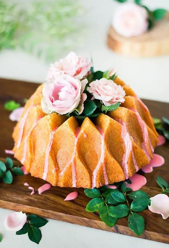 a creatively shaped bundt wedding cake with pink drip, pink blooms and greenery on top for a refined garden wedding