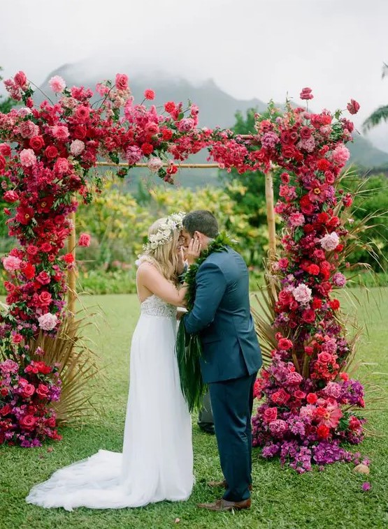 an extremely lush and colorful floral wedding arch covered with red, pink, purple blooms and some gilded leaves