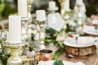 a beautiful enchanted forest wedding table setting with a moss runner, wood slices, pillar candles, greenery, wood slice placemats and neutral napkins