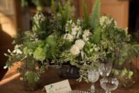 a beautiful enchanted forest wedding tablescape with neutral blooms, lots of textural greenery, green napkins, a clear charger and gold cutlery
