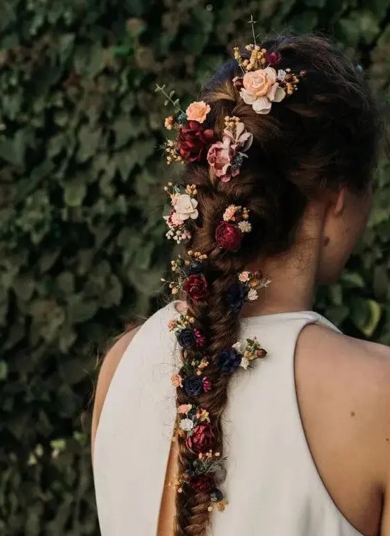 a beautiful thick and long fishtail braid with burgundy, pink and black blooms tucked in for a fall boho bride