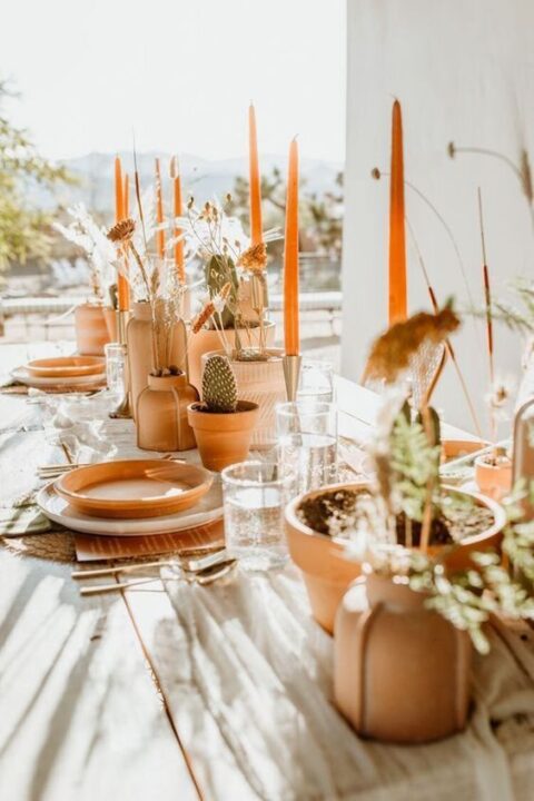 a boho sustainable micro wedding reception with terracotta vases, planters and plates, woven placemats and gold cutlery