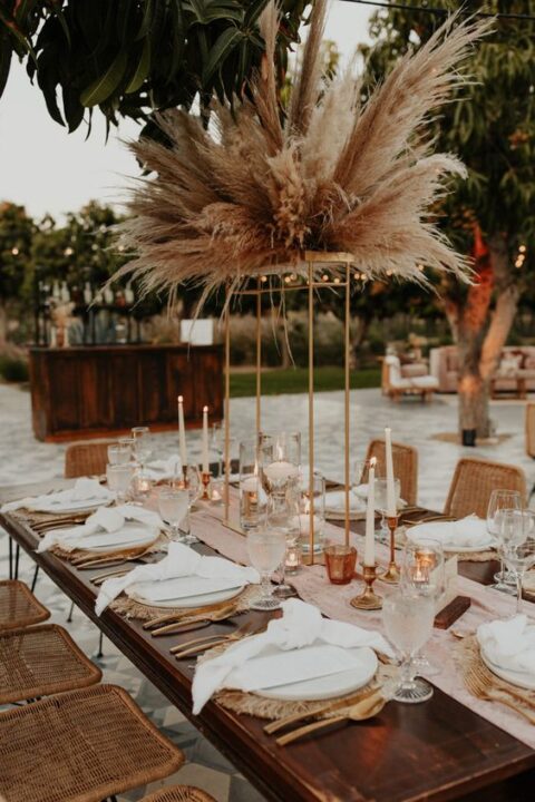 a boho tropical micro wedding tablescape with woven mats, a blush runner, a pampas grass centerpiece, gold cutlery and candles