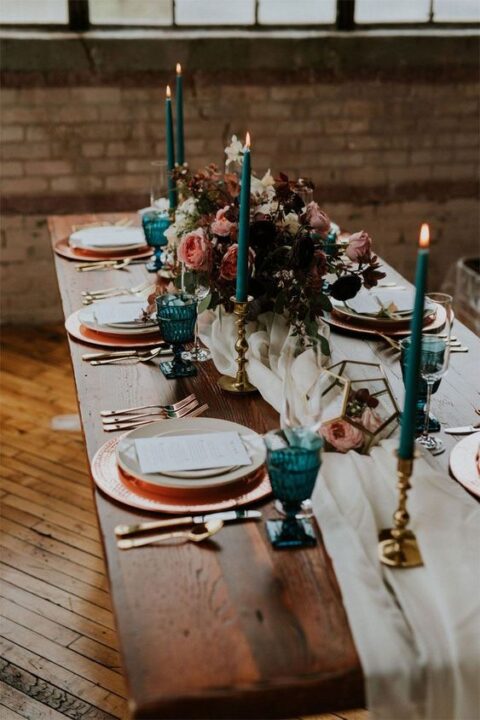 a bold and sophisticated micro wedding tablescape with teal candles and glasses, copper chargers and a pink and burgundy floral arrangement