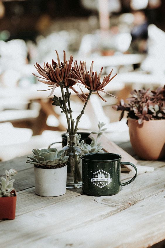 a bold eclectic wedding centerpiece of potted succulents, some blooms in a bottle and a tin mug is awesome