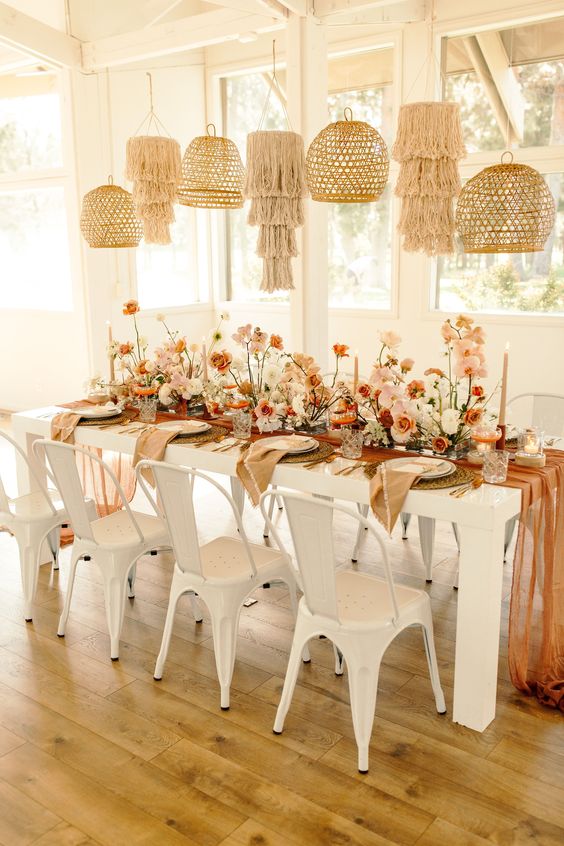 a bright boho wedding reception with a rust-colored table runner, rust and blush blooms, blush candles and boho pendant lamps