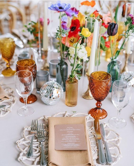 a bright eclectic wedding centerpiece of a disco ball, colorful bottles and vases, bold blooms and greenery is amazing
