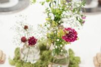 a bright eclectic wedding centerpiece of moss, wood slices, bottles with neutral and burgundy blooms and greenery