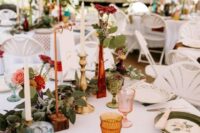 a bright enchanted forest wedding tablescape with floral print plates, a greenery runner, gilded candleholders, red and pink blooms