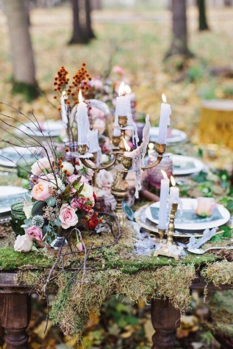a chic fall enchanted forest wedding tablescape with a moss runner, pink blooms, greenery and berries, a chic candelabra with thin and tall candles