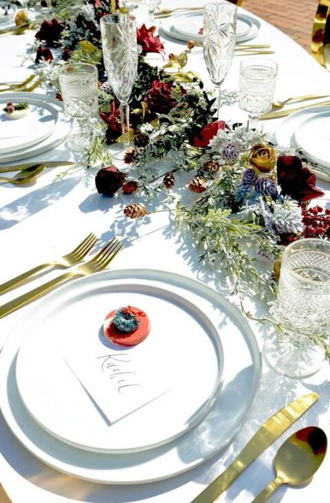 a colorful micro wedding table with a bold fresh and dried flower runner, white plates, gold cutlery and elegant glasses