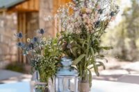 a cozy wedding centerpiece of a wood slice, a hurrican lantern, jars with wildflowers and thistles and a small candle