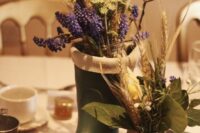 a creative wedding centerpiece of rubber boots with bold blooms and grasses, a jar with burlap and some leaves and grass
