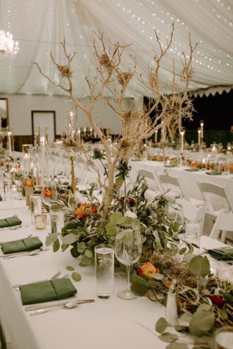 a fab indoor enchanted forest wedding reception space with neutral and green linens, greenery, bright blooms and thistles, a mini tree and candles