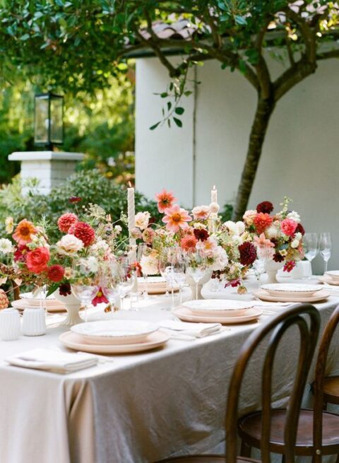 a fabulous micro wedding tablescape with pink and red centerpieces, candles, neutral plates is a beautiful idea