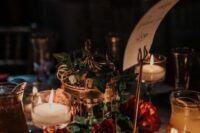 a fantastic enchanted forest wedding reception table with a wood slice, a cage with greenery and burgundy roses, candles and a table name