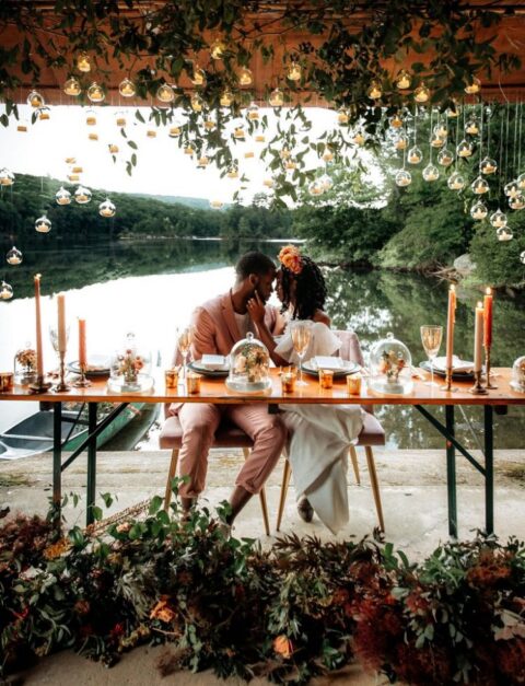a gorgeous boho wedding reception with lush greenery and blooms, with candle bubbls hanging down, with a fantastic view of the lake