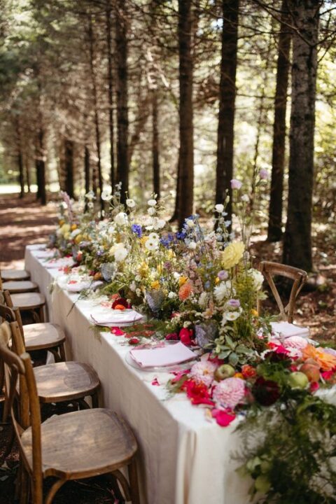 a gorgeous enchanted forest wedding tablescape with bright blooms, greenery and moss, clear chargers and neutral napkins