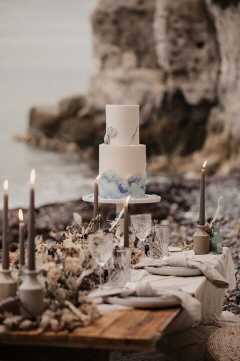 a lovely coastal micro wedding tablescape with grey candles in grey candleholders, a dried flower runner, grey plates and neutral linens
