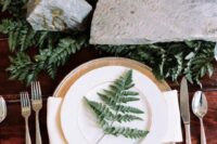 a lovely enchanted forest wedding tablescape with ferns, large rocks including a gilded rock, a metallic charger and white plates