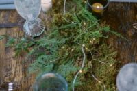 a lovely enchanted woods wedding tablescape with a moss and fern runner, lights and candles, elegant glasses and grey napkins