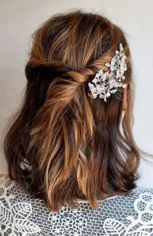 a messy textural half updo with a twisted part secured with a rhinestone floral hairpin for a romantic touch