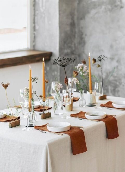 a modern fall micro wedding tablescape with orange candles and rust napkins, white plates and lots of dried flowers