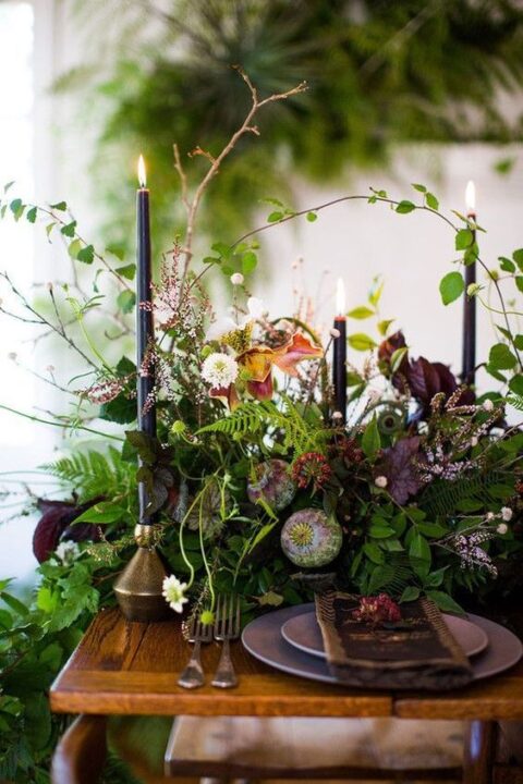 a moody wedding tablescape with greenery, dark blooms, black candles, seed pods and deep purple porcelain is a very chic idea for an enchanted forest wedding